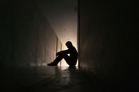 Depressed Person Sitting Alone in dark hallway